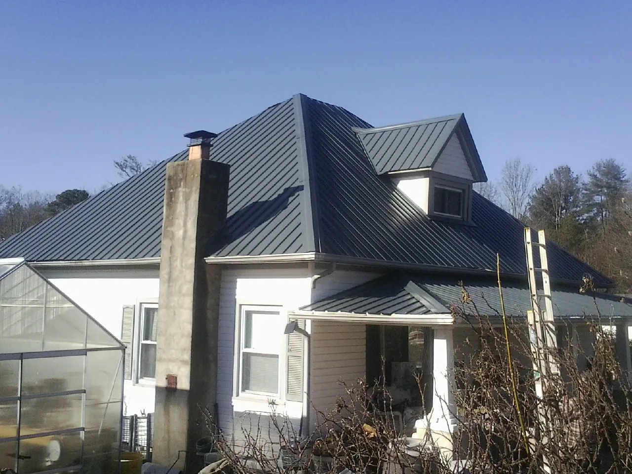 Dark blue standing seam metal roof on a white farmhouse with dormer — Slate & Tile Roof Repair by Roofing Brothers in Jerico Springs