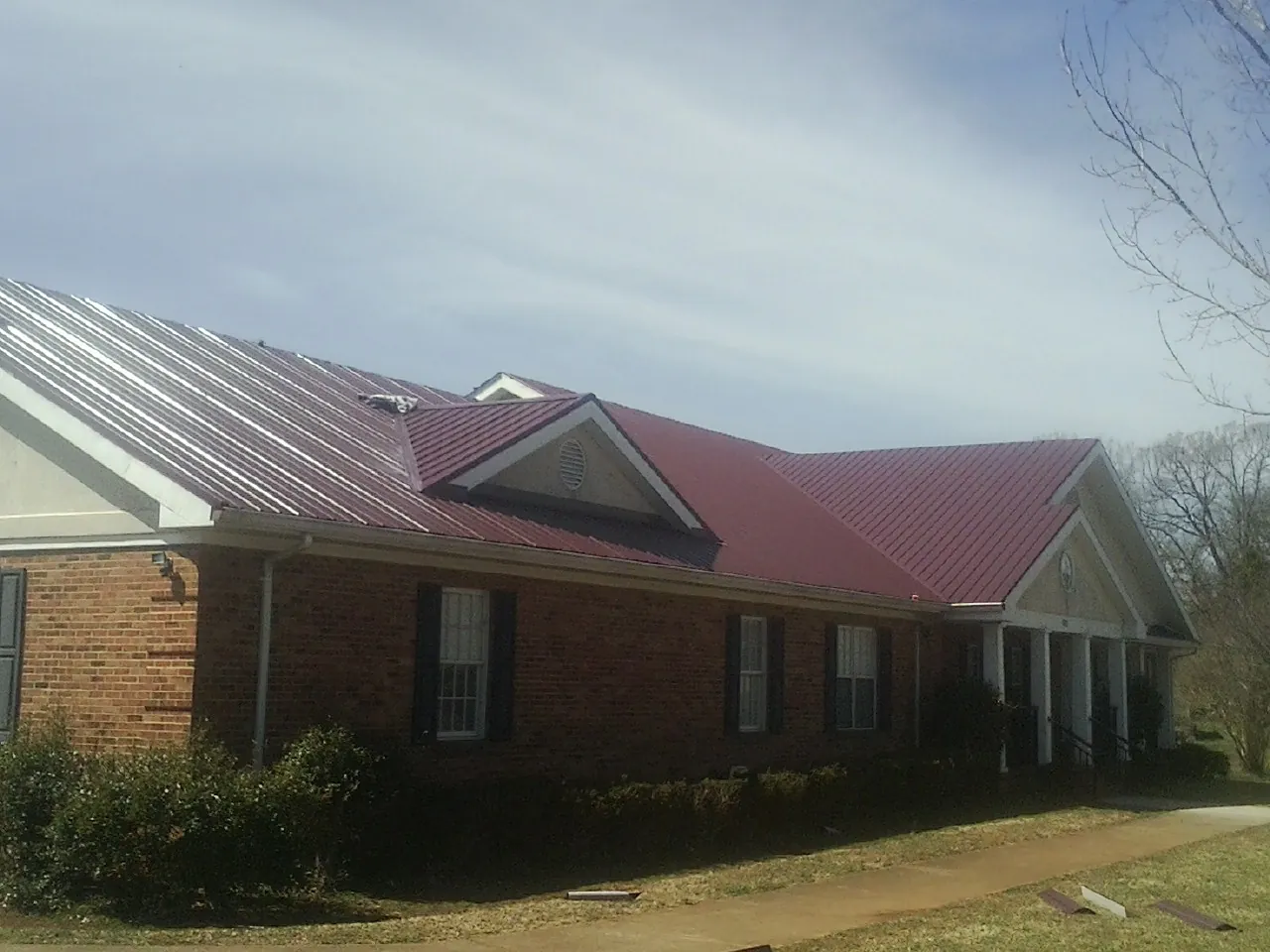 Red metal roof with gabled entries on a long brick building, from a Hail Damage Roof Repair job in Jerico Springs