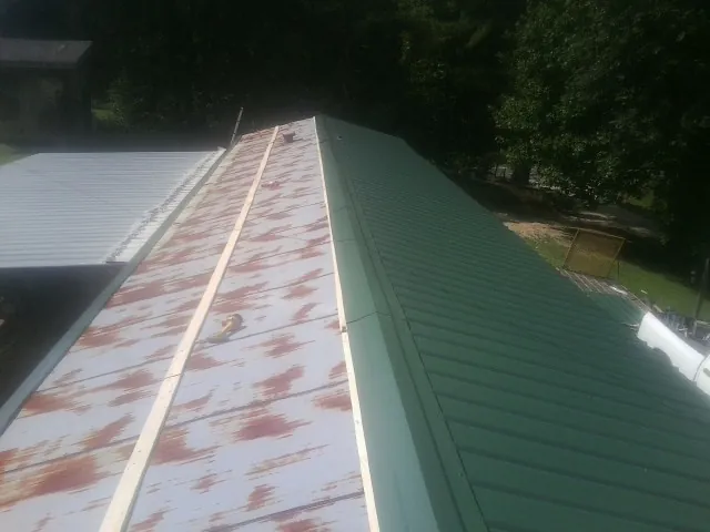 Old rusted panels beside newly installed green metal roofing — Wind Damage Roof Repair by Roofing Brothers in Jerico Springs