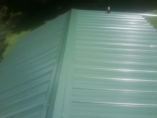 New green metal panels meeting at the ridge of a roof — Flat Roof Repair work by our crew in Jerico Springs