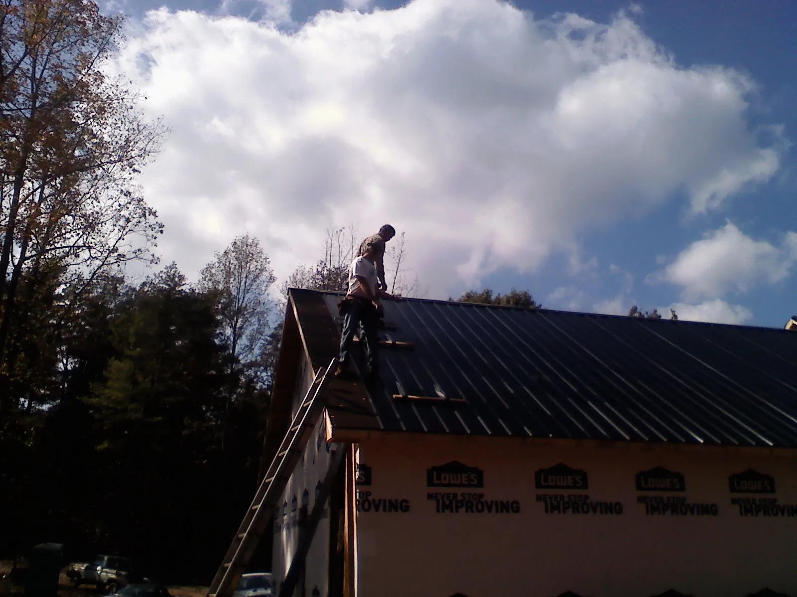 Roofer fastening dark metal panels high against a cloudy sky, from a Roof Inspection job in Jerico Springs