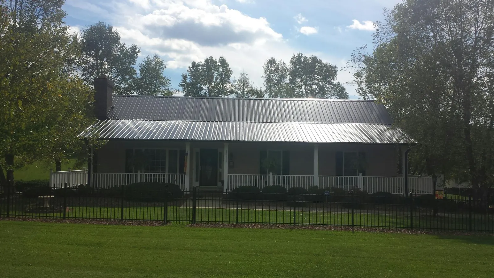 Gray metal roof on a brick ranch with a full width front porch — Gutter Guard Installation work by our crew in Jerico Springs