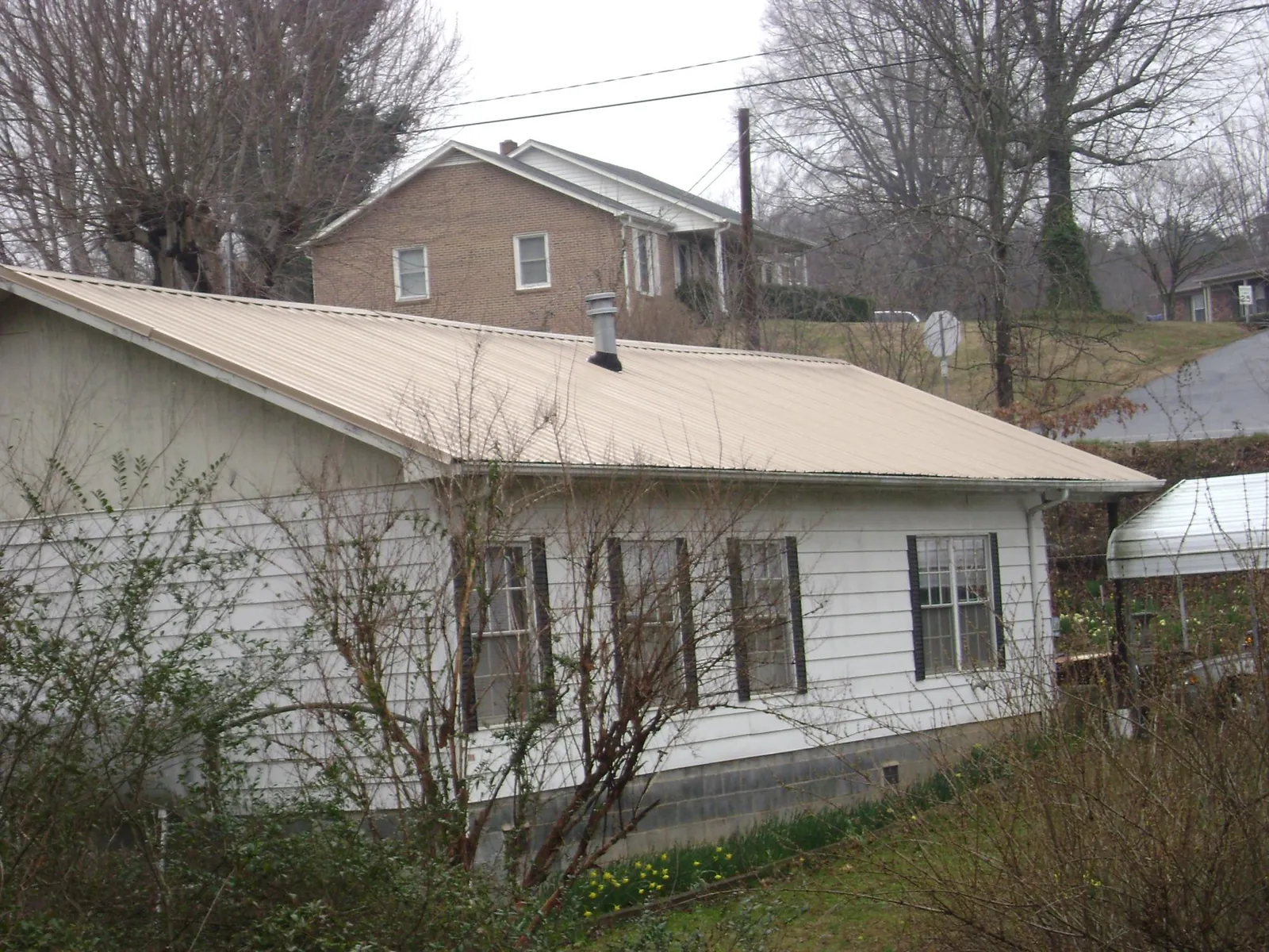 Tan metal roof on a white sided house set into a hillside — Commercial Roofing by Roofing Brothers in Jerico Springs