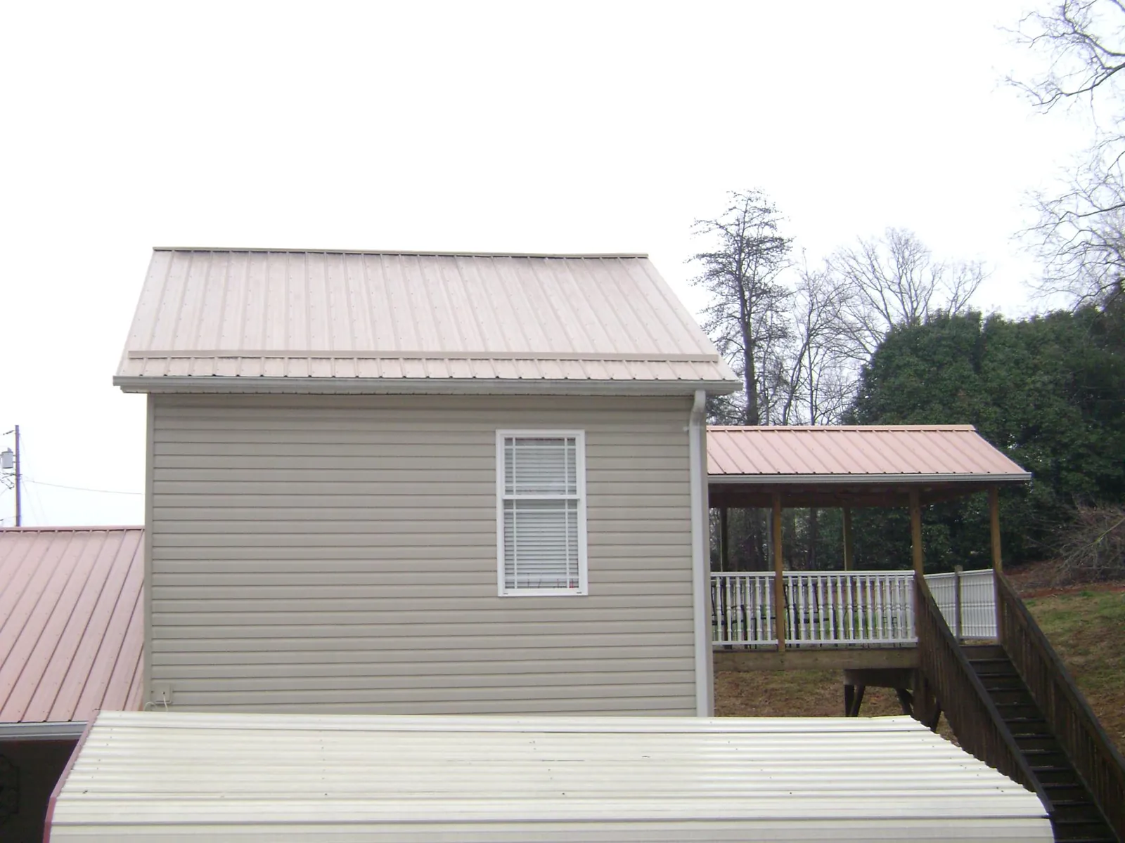 Tan metal roofs on a two story addition and attached porch, from a Roof Replacement job in Jerico Springs